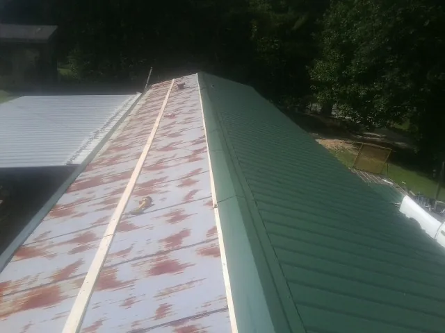 Old rusted panels beside newly installed green metal roofing in Acme
