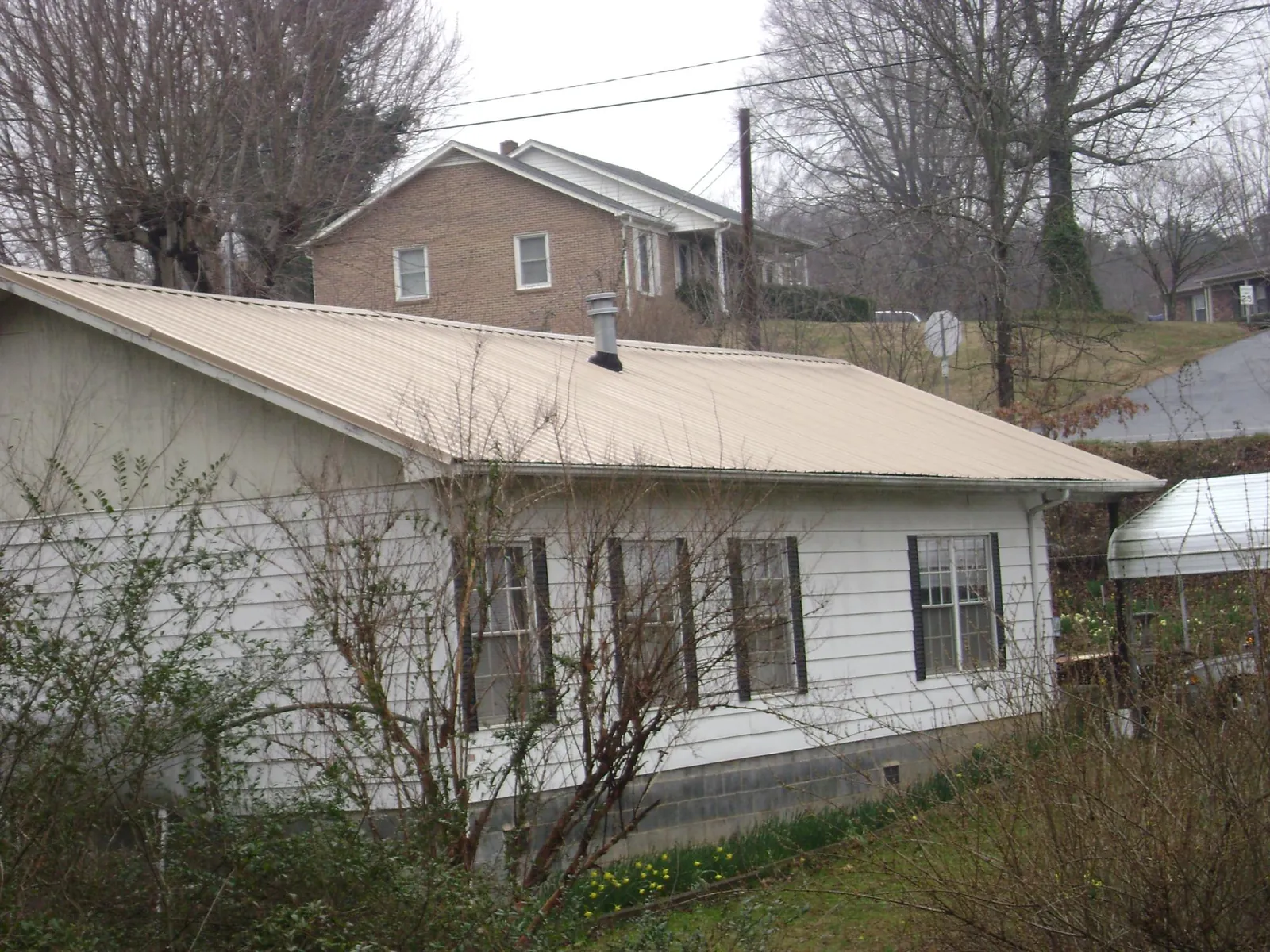 Tan metal roof on a white sided house set into a hillside — Commercial Roofing by Roofing Brothers in Acme